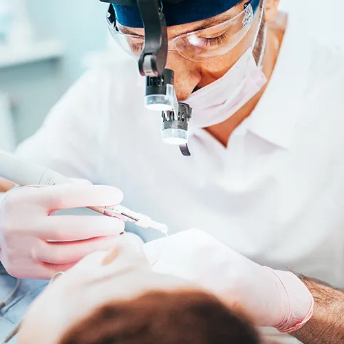 dentist wearing glasses working in a reclining patient's mouth with dental tools