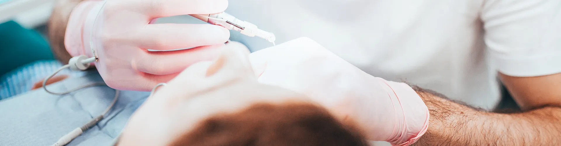 dentist wearing glasses working in a reclining patient's mouth with dental tools