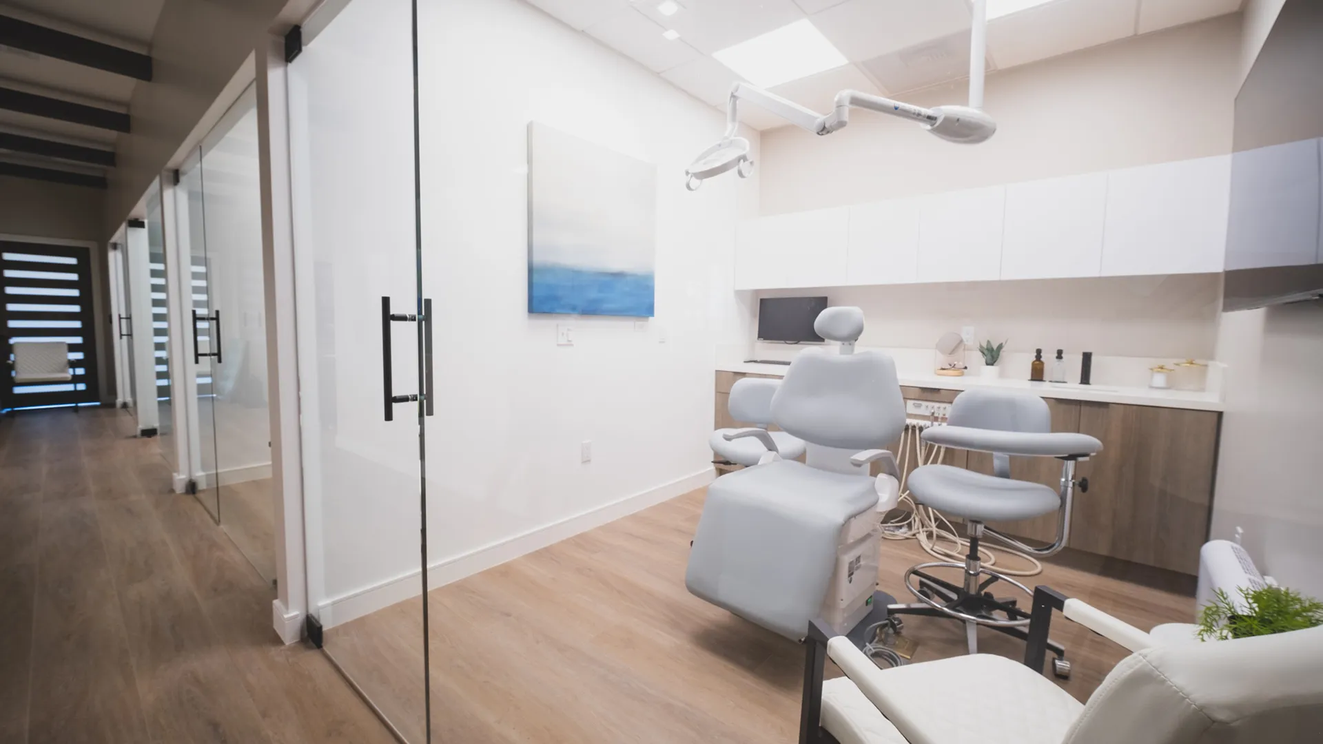 Glass-enclosed dental treatment room at Aviara Centers with patient chair, exam light, consultation seating, and hallway view