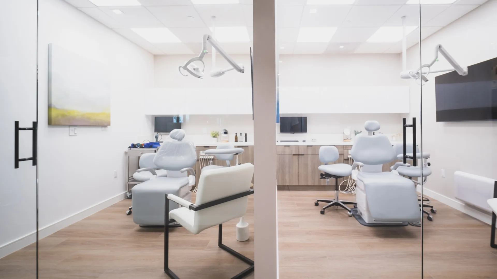 Dual glass-enclosed dental treatment rooms at Aviara Centers with patient chairs, exam lights, consultation seating, and wall-mounted screens