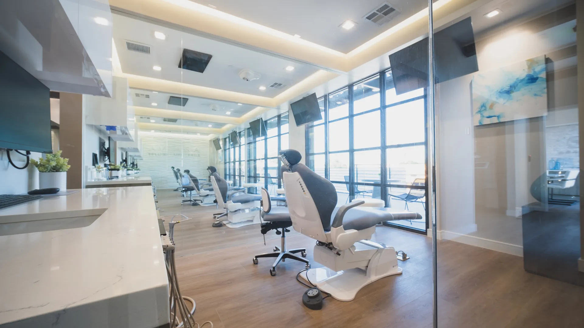 Open dental treatment area at Aviara Centers with multiple operatories, reclining patient chairs, wall-mounted screens, and floor-to-ceiling windows