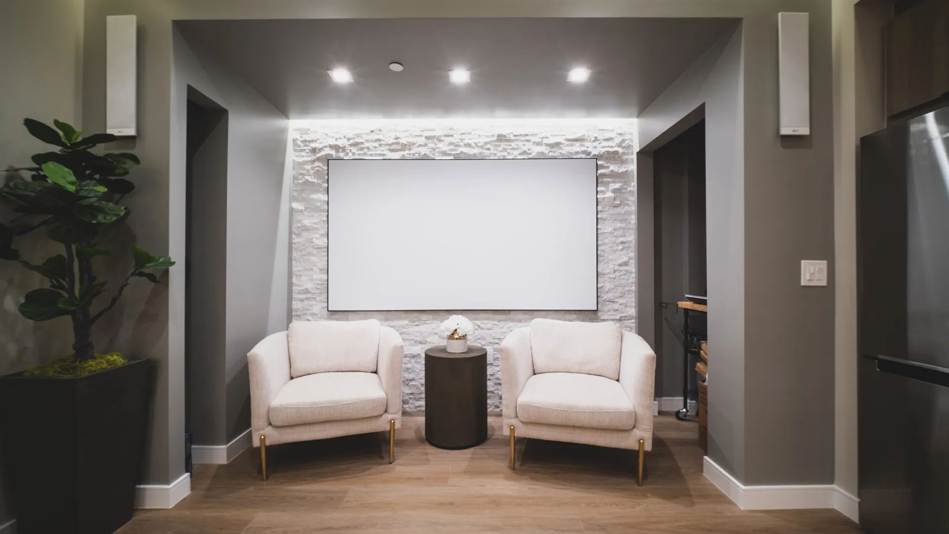 Patient lounge at Aviara Centers with two upholstered chairs, stone feature wall, and large presentation screen