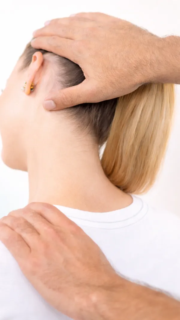 A practitioner’s hands gently support a woman’s head and shoulder as she tilts her neck back, shown in a soft, bright clinical-wellness setting.