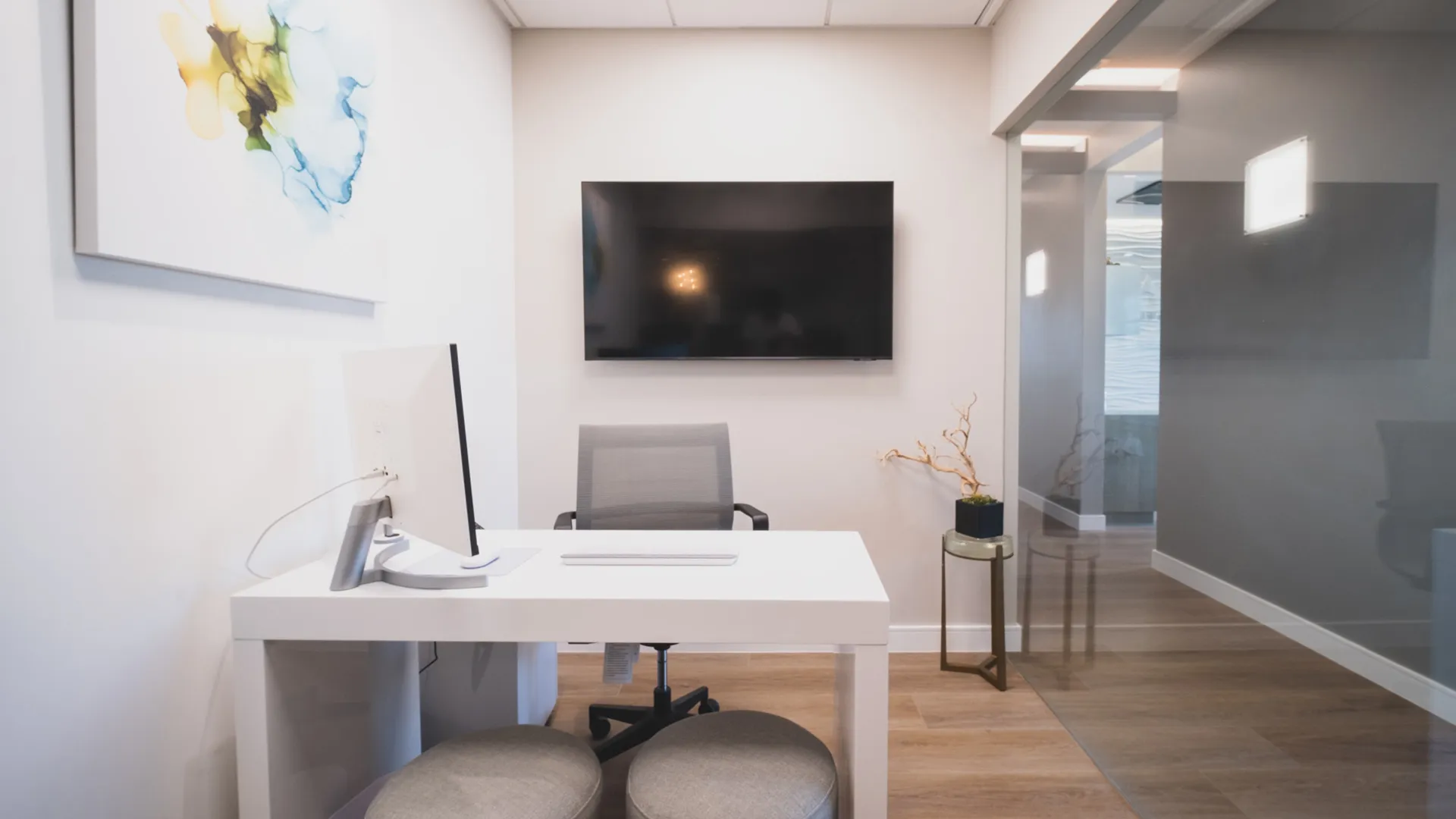 Private consultation office at Aviara Centers with desk, computer workstation, wall-mounted screen, and glass hallway entry