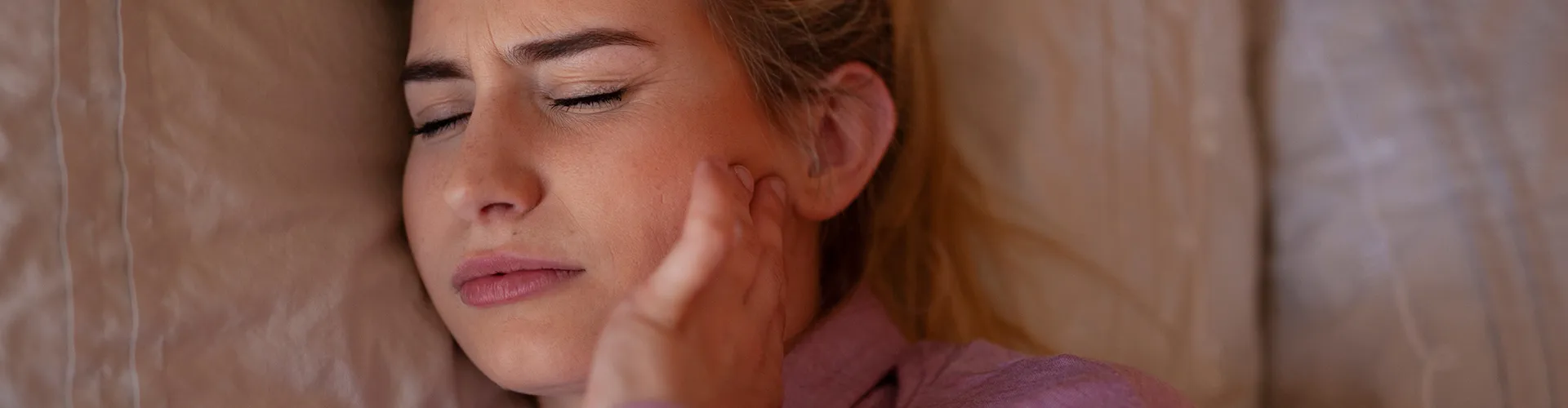 female laying in bed holding her jaw